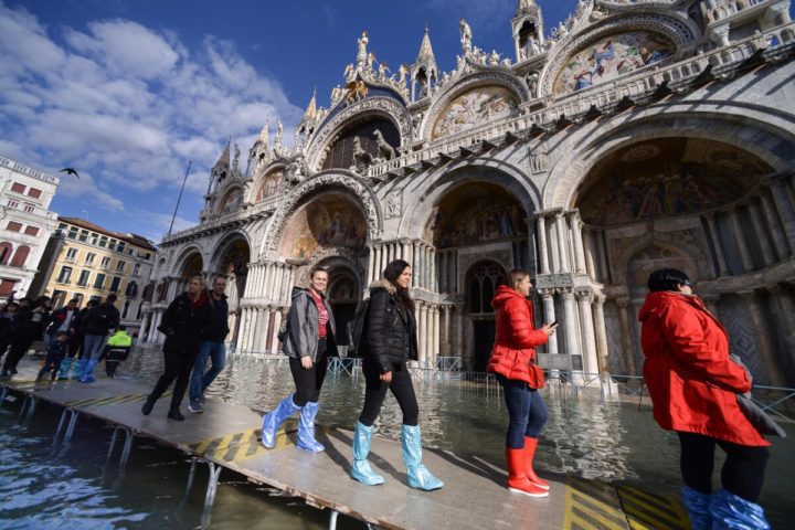 People walk on a footbridge across the flooded St. Mark's Square by St. Mark's Basilica on November 14, 2019 in Venice. - Much of Venice was left under water after the highest tide in 50 years ripped through the historic Italian city, beaching gondolas, trashing hotels and sending tourists fleeing through rapidly rising waters. (Photo by Filippo MONTEFORTE / AFP)
